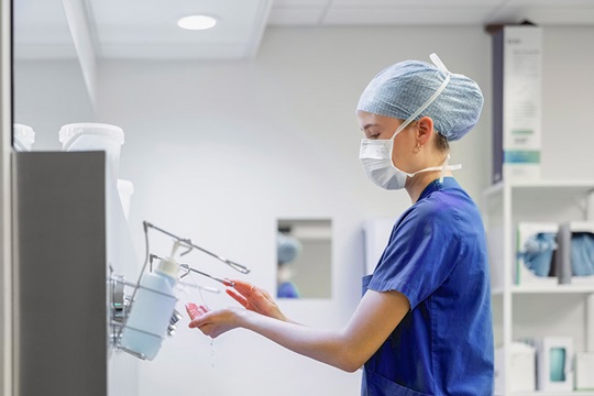 Nurse in surgical scrubs disinfects her hands.